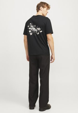 Zwarte katoenen t-shirt met een grafische print met bloemen en tekst op de achterkant. Ontspannen pasvorm gecombineerd met zwarte wijde broek en laarzen.