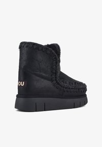 Bota negra de tobillo hecha de suave ante con costuras en contraste, una superficie texturizada y una suela de goma negra resistente.