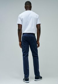 Pantalones vaqueros azul marino con un corte ajustado y tejido texturizado, con bolsillos traseros y una cinturilla elástica, combinados con una camiseta blanca lisa.