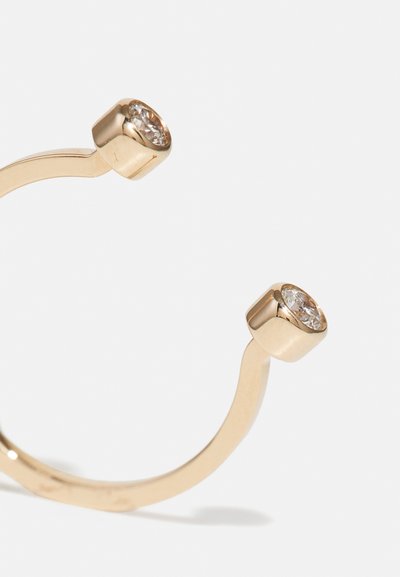 Goldring mit geschwungenem Design, ausgestattet mit zwei klaren, runden Edelsteinen, die in strukturierten, sechseckigen Krappen auf beiden Enden eingefasst sind.
