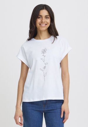 Donna sorridente con lunghi capelli scuri che indossa una maglietta bianca con un disegno lineare minimalista di una rosa e la parola "amore", abbinata a un paio di jeans blu.