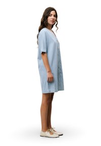 Hellblau gestreiftes Kleid mit kurzen Ärmeln, durchgehender Knopfleiste, knielangem Schnitt und seitlichen Taschen. Tragen mit beigen Schnürschuhen.