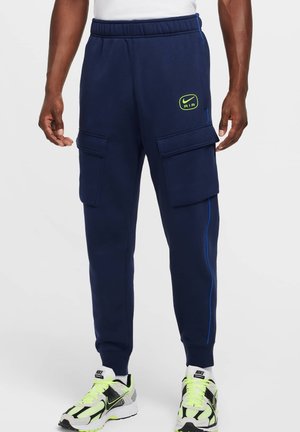 Navy sweatpants with cargo pockets, elastic waistband, blue side stripes, and green Nike logo. Features a soft, textured fabric.