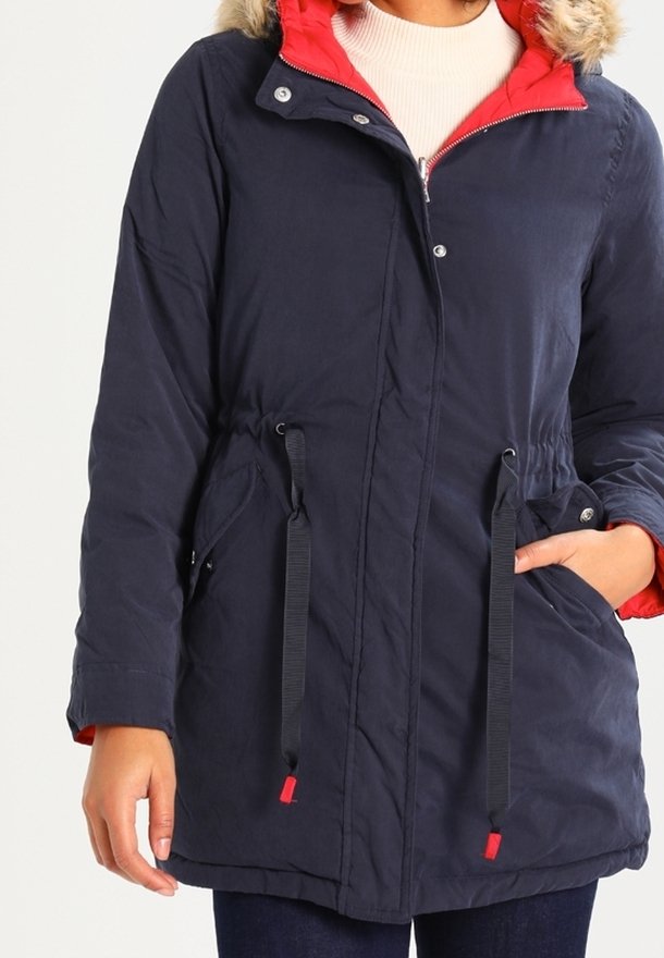 Námořnická modrá parka s červenou podšívkou, umělou kožešinou na kapuci, stahovacími pasem a bočními kapsami. Obsahuje zapínání na patentky.