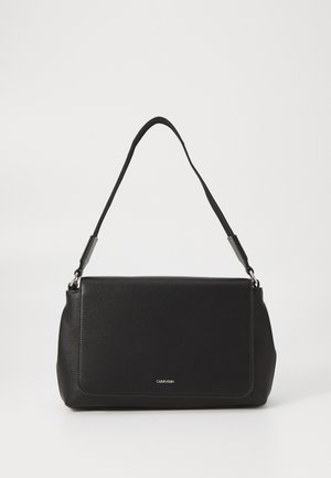 Sac d'épaule rectangulaire noir Calvin Klein avec une sangle unique et une fermeture à rabat sur un fond clair uni.