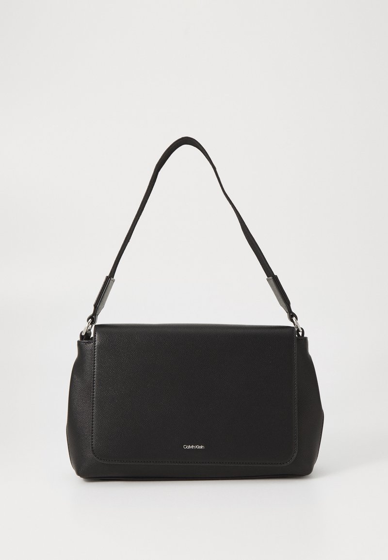 Sac d'épaule rectangulaire noir Calvin Klein avec une sangle unique et une fermeture à rabat sur un fond clair uni.