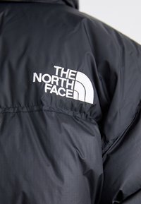 Veste noire matelassée avec logo The North Face blanc brodé sur le haut du dos.