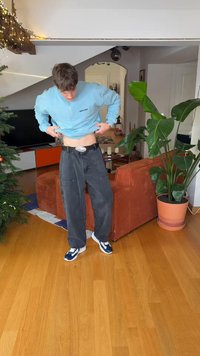 Ανοιχτό μπλε φούτερ με φερμουάρ, μαύρο τζιν παντελόνι φαρδιάς γραμμής με τσέπες, ασημένια αγκράφα ζώνης και λευκά αθλητικά παπούτσια με μπλε λεπτομέρειες.