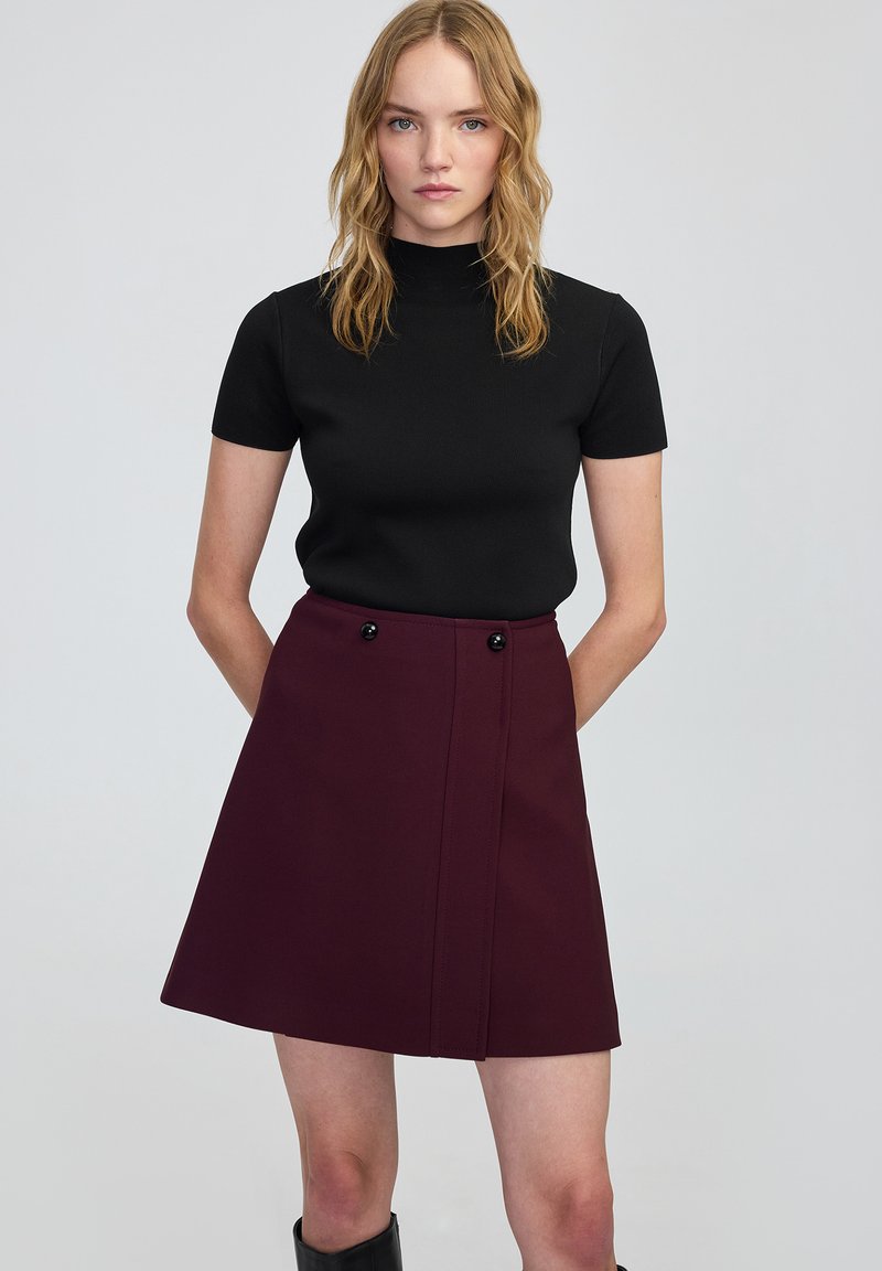 Zwart top met korte mouwen, gecombineerd met een hooggewaaid bordeauxrok met een voorpaneel, twee zwarte knoopaccenten en een rechte zoom.