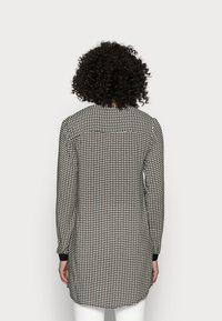 Tunique à manches longues avec un motif géométrique noir et blanc, présentant un ourlet arrondi et des poignets noirs. Vue arrière avec un détail de emmanchure contrastant.