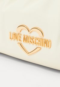 Bijela kožna torba s zlatnim logotipom "LOVE MOSCHINO" unutar oblika srca, s glatkom teksturom i minimalističkim dizajnom.