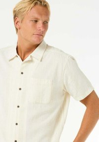 Kortærmet, cremefarvet skjorte med knapper, der har et subtilt tekstureret mønster, brystlomme og brune knapper. Casual pasform med standard krave.