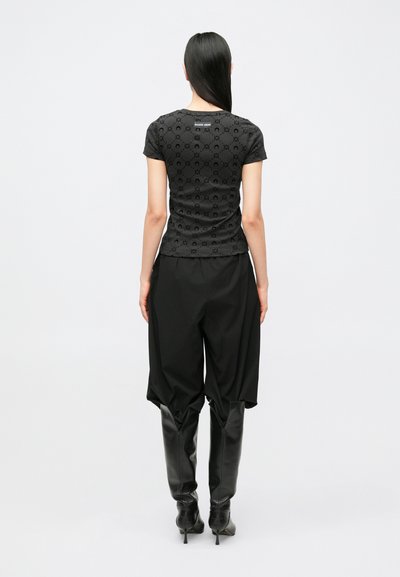 Top preto justo com padrão texturizado, mangas curtas e decote redondo, combinado com calças pretas largas e botas até ao joelho.