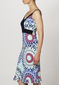 Sovel dress ilman hihoja, jossa on musta yläosa ja värikäs geometrinen kuvio sinisen, punaisen ja valkoisen sävyissä, sekä röyhelöhelma.