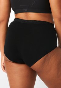 Slip in cotone nero a vita alta con bordo scallopato. Tessuto liscio e senza motivi o dettagli hardware visibili.