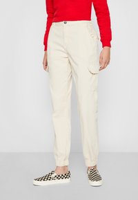 Beige cargo pants with elastic cuffs and pockets; paired with black and white checkered slip-on shoes and a red long-sleeve top.