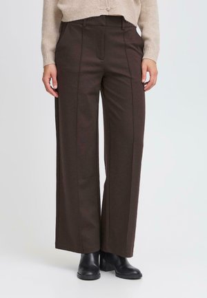 Braune weit geschnittene Hosen aus weichem Stoff, mit vorderen Falten, hoher Taille und seitlichen Taschen. Kombiniert mit schwarzen Knöchelstiefeln.