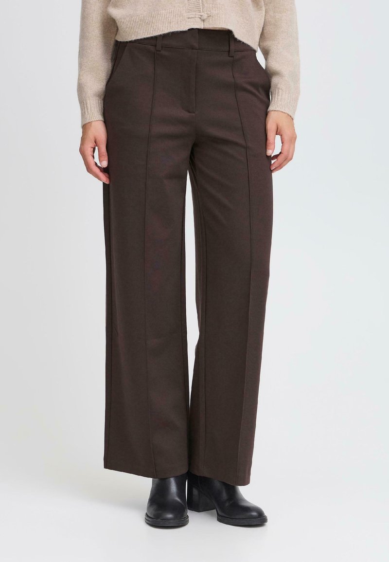Pantalons larges marron en tissu doux, dotés de plis sur le devant, d'une taille haute et de poches latérales. Associés à des bottines noires à talons.
