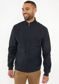 Giubbotto bomber nero con un colletto alto, zip frontale e due grandi tasche applicate. Realizzato in un tessuto liscio e leggero con polsini a coste.
