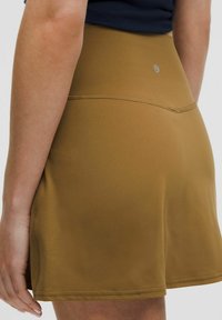 Barna sportos szoknya sima anyagból, magas derékkal és varrási részletekkel. Színében egységes, minta nélkül.