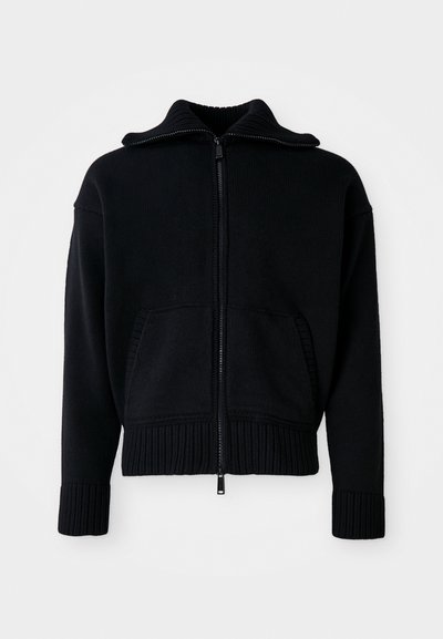 Maglione zip-up nero con texture a coste, colletto alto e due tasche frontali. Presenta ampi polsini e orlo a coste. Design minimalista.