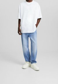 Vit bomull t-shirt med avslappnad passform, kombinerad med ljusblå jeans med avslappnad passform och vita sneakers. Enkel design, inga synliga mönster.