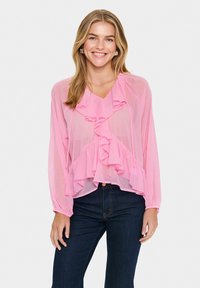 Blouse légère et rose avec des détails froncés, décolleté en V et manches longues. Assortie à un jean foncé, elle possède une silhouette ample et fluide.