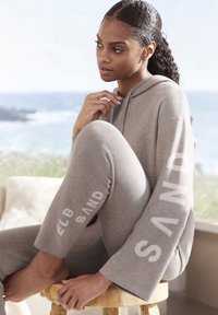 Hellgraues Loungewear-Set mit Kapuzenpullover mit weiten Ärmeln und figurbetonten Leggings mit weißen Schriftzügen an den Seiten.