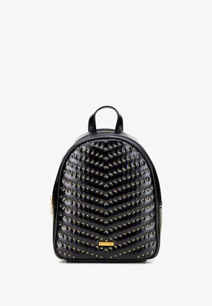 Mochila de cuero negro con textura acolchada y tachuelas doradas. Presenta una forma redondeada, asa superior y cierre de cremallera. Detalle del logo dorado en la parte frontal.