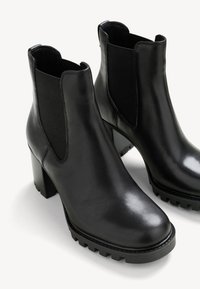 Černé kožené kotníkové boty s elastickými bočními panely, robustní texturované podpatky a hladkým povrchem. Vystužené gumové podrážky pro lepší přilnavost.