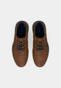 Pruunid nahast kingad siniste paeltega, ümara varbaosaga, õmmeldud detailidega ja kontrastse tallaga. Mõeldud vabama väljanägemise jaoks, sileda viimistlusega.