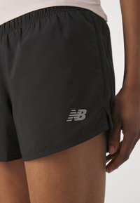 Black athletic shorts made of lightweight fabric, featuring an elastic waistband and a reflective New Balance logo on the lower side.