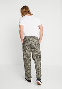 Leopard print pants made of lightweight fabric, featuring a loose fit, elastic waistband, and subtle pockets. Paired with a white t-shirt.