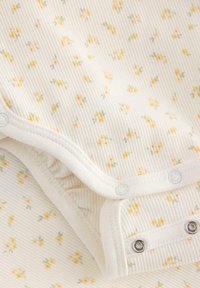 Bomulds baby bodystocking med ribbet tekstur, cremet bund og spredt gult blomsterprint. Har trykknaplukning i bunden.