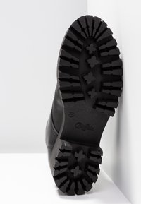 Černá podrážka boty s hlubokým, robustním vzorem. Materiál vypadá gumově s drážkami pro zvýšení trakce a vyraženým logem.