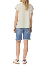 Licht beige kort shirt met korte mouwen, blauwe denim shorts met opgerolde zoom, en witte sneakers met zwarte accenten op de hiel.