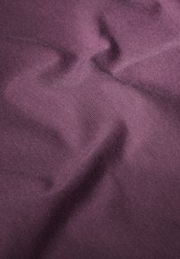 Lila texturerad tyg med ett subtilt diagonalt ribbmönster, som visar varierande nyanser och en mjuk, slät finish.