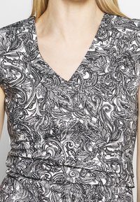 Haut à motif cachemire noir et blanc avec un col en V, manches courtes et tissu texturé, silhouette près du corps.