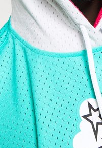 Een mintgroene hoodie gemaakt van mesh-stof, met contrasterende witte accenten, een sterafbeelding en gestructureerde stikdetails.