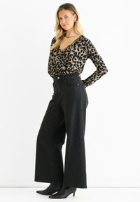 Top a maniche lunghe con stampa leopardata abbinato a jeans neri a vita alta con gamba ampia e stivaletti neri con tacco. Tessuto morbido e vestibilità su misura.