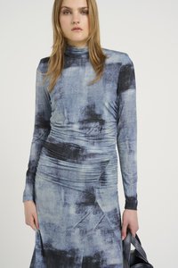 Vestido de mangas compridas em estampado abstrato azul e preto, com detalhes franzidos, tecido suave e silhueta ajustada.