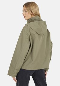 Giacca con cappuccio verde oliva realizzata in materiale leggero, caratterizzata da una vestibilità comoda e un design semplice senza hardware visibile.