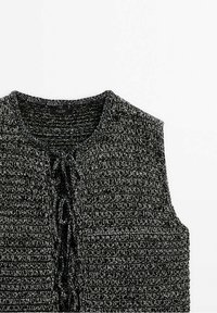 Czarna i szara dzianinowa bluzka bez rękawów z teksturowanym wzorem i detalem z przodu do związania. Okrągły dekolt i otwarty krój.