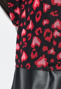 Blusa negra transparente con estampado de leopardo rojo y rosa. La parte inferior presenta cuero negro, añadiendo contraste en textura y color.