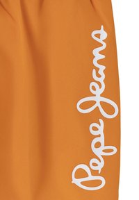 Oranžinės šortai, pagaminti iš lygaus audinio, su dideliu baltu logotipu, užrašu "Pepe Jeans", spausdintu vertikaliai ant šono.