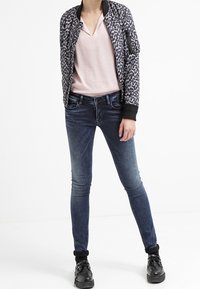 Chaqueta bomber de estampado de leopardo sobre una blusa rosa claro, combinada con jeans ajustados azul oscuro y zapatillas negras. Diseño ajustado, tejido suave.