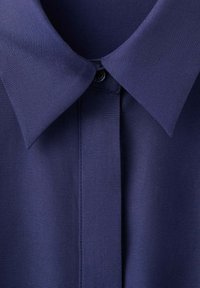 Col de chemise bleu marine avec patte boutonnée, montrant une texture de tissu lisse et des pointes de col pointues.