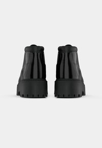 Stivali alla caviglia neri con finitura lucida, suola spessa nera e battistrada resistente. Il design presenta una punta rotonda e un collare imbottito per un maggiore supporto.