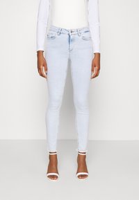 Jeans skinny de color azul claro con una cintura alta, cuentan con bolsillos delanteros y un dobladillo deshilachado. Combinados con sandalias de tacón blancas con tiras.