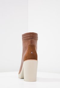 Bottine en cuir marron avec des panneaux en daim, large talon blanc, et couture décorative. Patch logo à l'arrière près du talon.